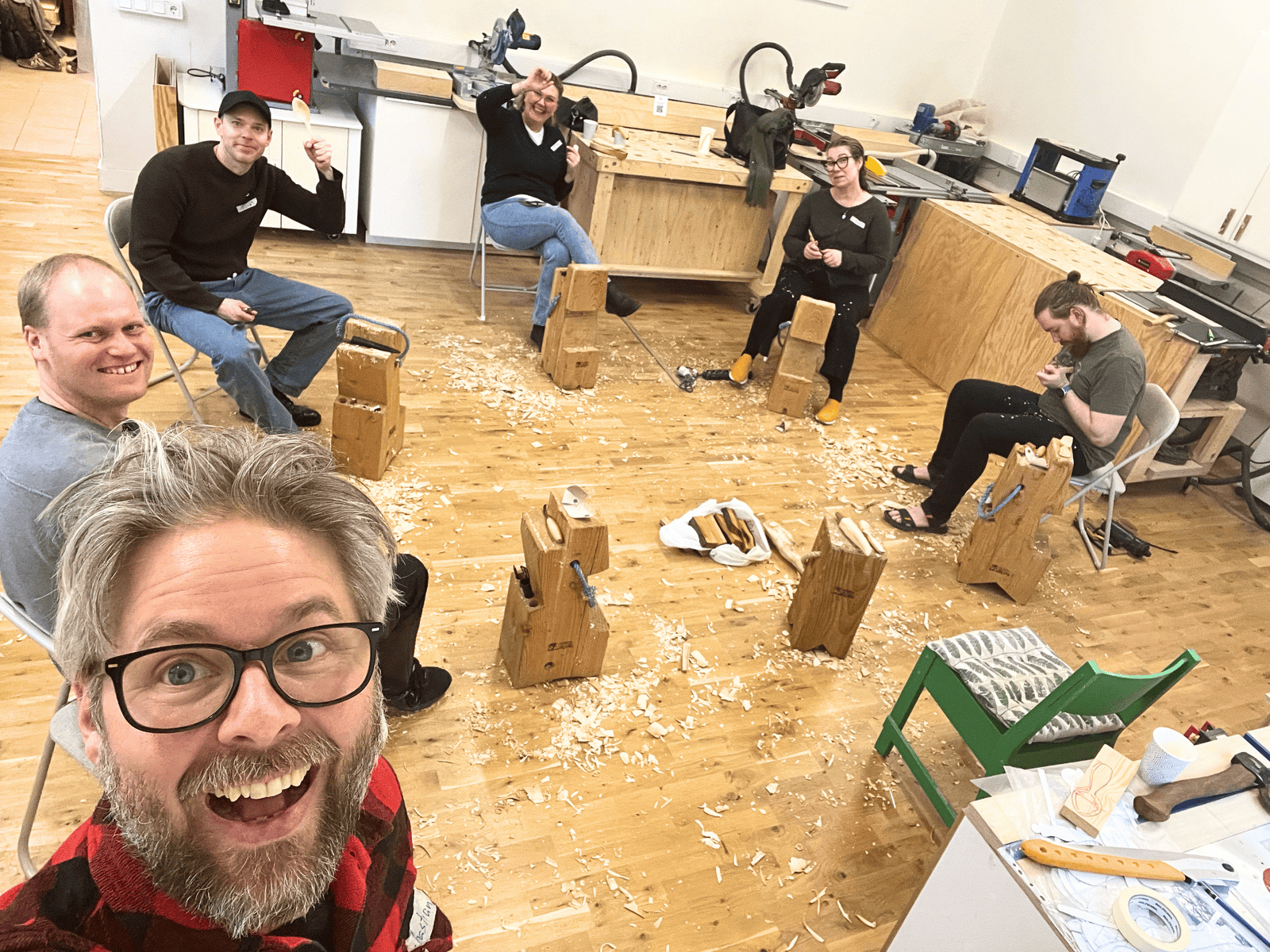 Creative woodworking workshop with six people collaborating and smiling. Group of six people working together on woodworking projects in a bright workshop.
