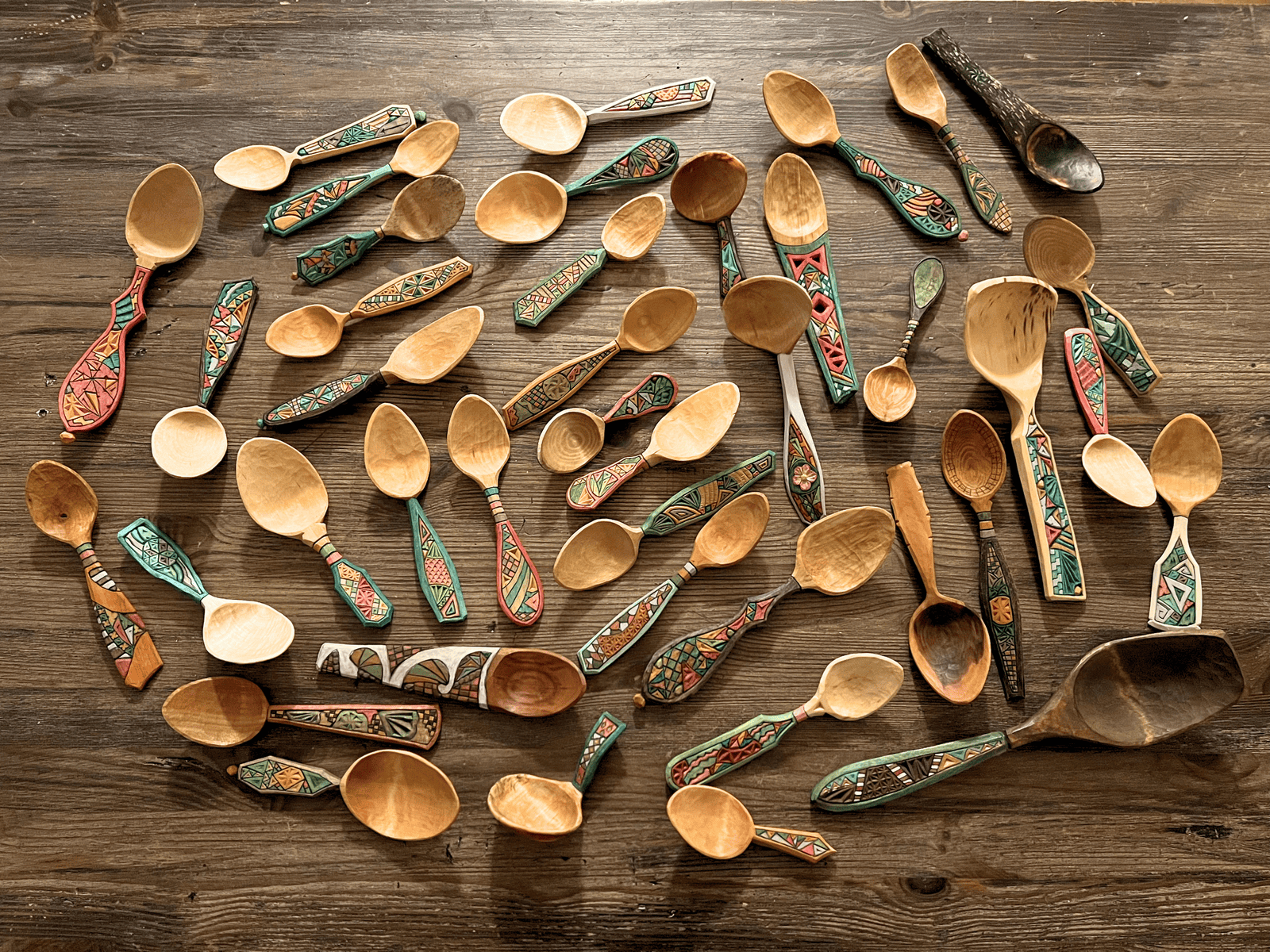 Colorful handcrafted wooden spoons arranged on a rustic wooden surface. Vibrant, artisan wooden spoons with intricate painted designs, perfect for kitchen decor or culinary.