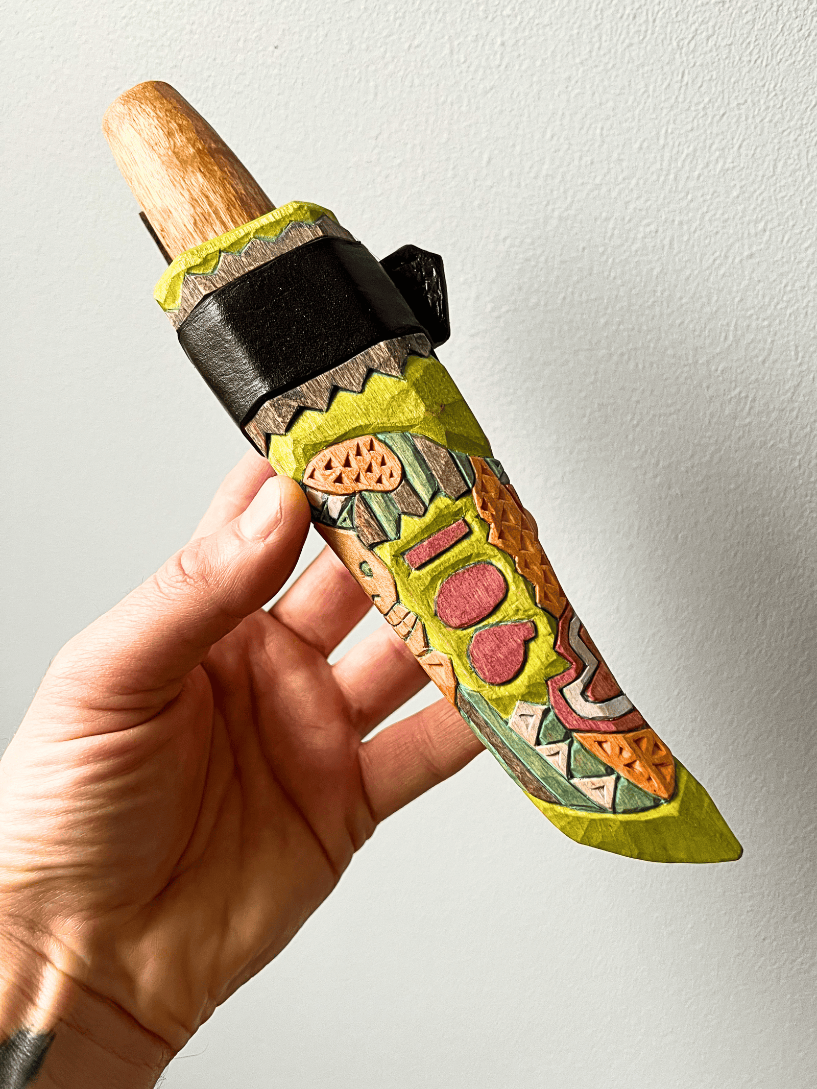 Wooden knife with carved colorful design, held in hand for display.